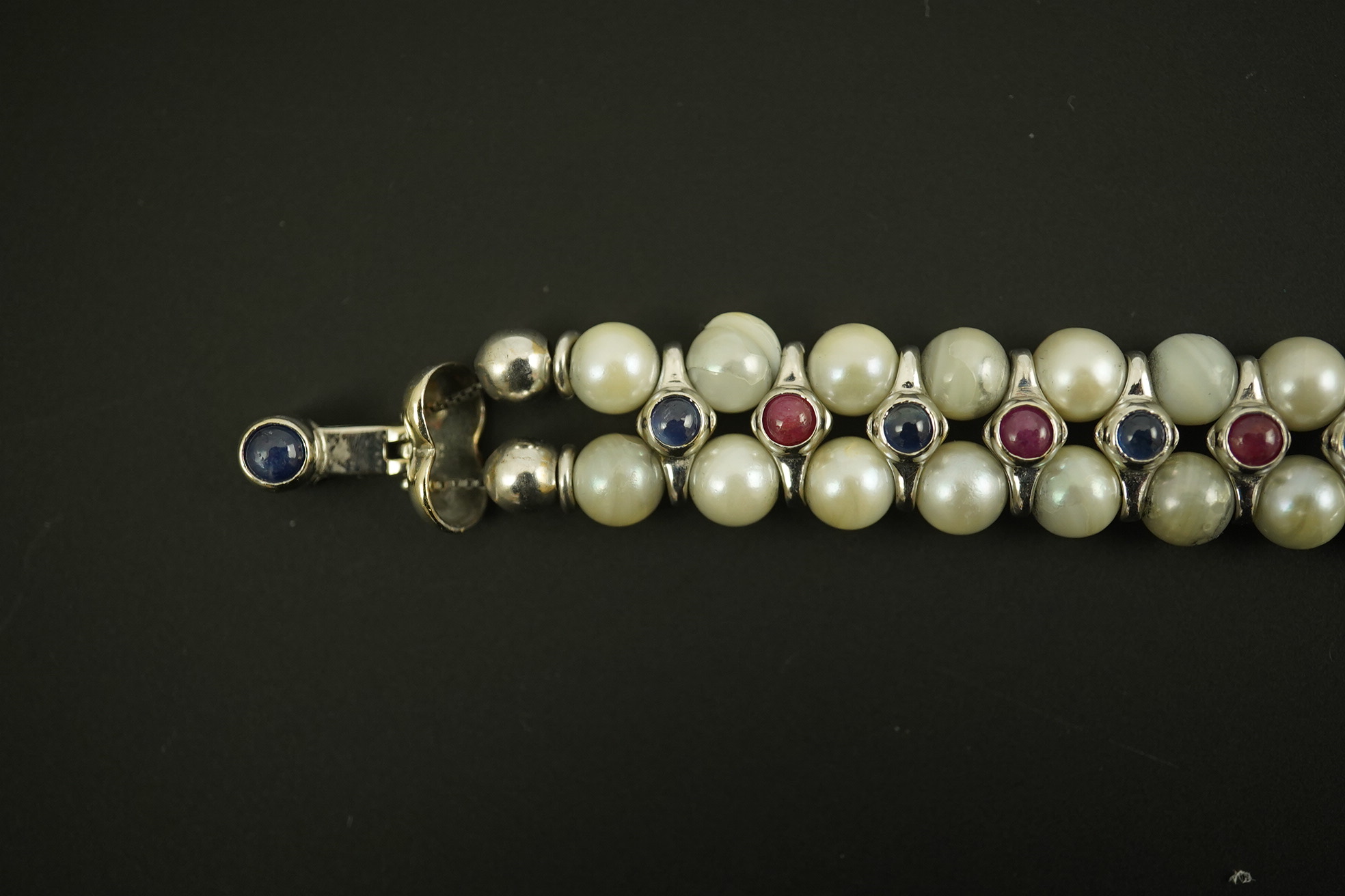 A late 20th century 18k white gold and two row cultured pearl bracelet, set with single row of cabochon rubies and sapphires